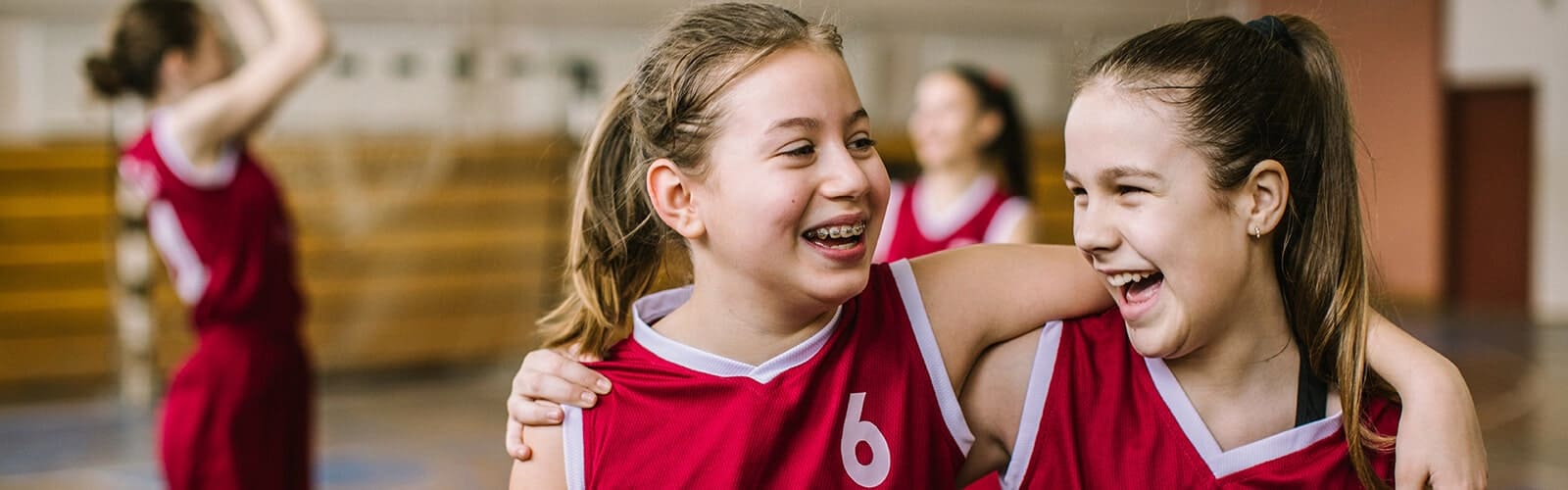 Two children wearing braces hugging each other while playing sport