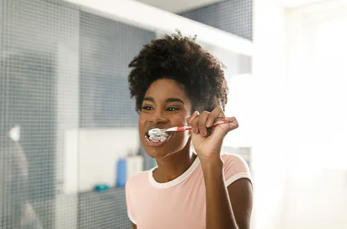 Girl brushing her teeth and braces in front of a bathroom mirror