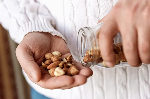 Person tipping a handful of nuts out of a jar