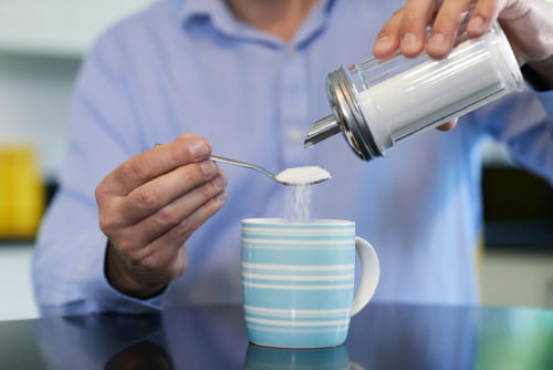 Man Adding Sugar To Hot Drink At Home