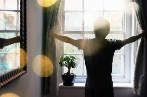 A man open his curtains to greet the sunny day. He's overcoming his fear of the orthodontists by scheduling his appointment first thing to stop him stressing about it all day