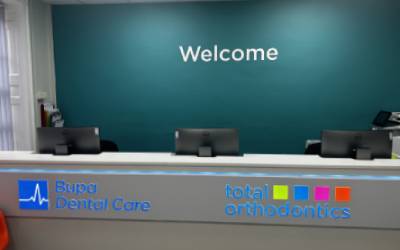 The reception of Total Orthodontics Kidderminster has a teal wall behind the desk with white lettering saying welcome